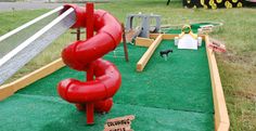 there is a red slide in the grass with some signs on it and a black dog standing next to it