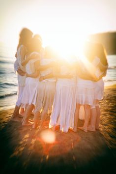 a group of women standing next to each other on top of a sandy beach near the ocean