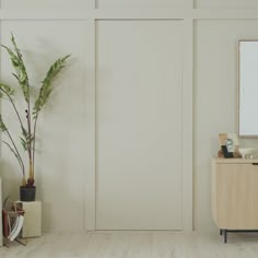 an empty room with white walls and a wooden cabinet next to a potted plant