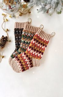 two knitted christmas stockings sitting on top of a white table next to pine cones