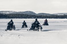 four people are riding snowmobiles in the snow