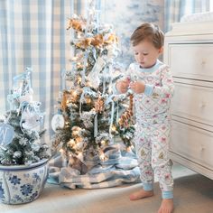 a little boy standing next to a christmas tree in front of a white chest of drawers