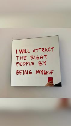 a person holding a cell phone in front of a white board with writing on it that says, i will attract the right people by being my self