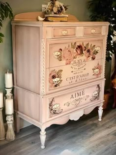 a pink dresser with flowers painted on the front and drawers, next to some candles