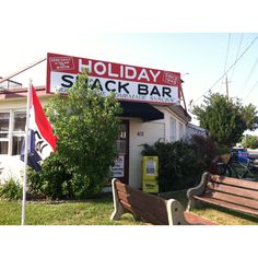 there is a sign that says holiday stack bar on the side of a building next to a park bench