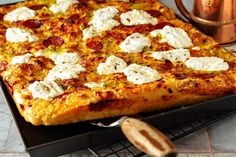 a square pizza sitting on top of a pan next to a copper cup and spoon