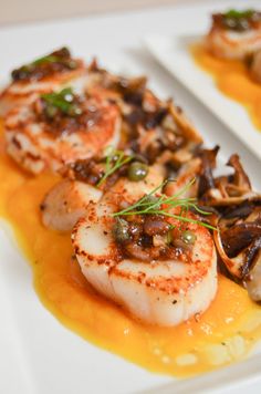 scallops and mushrooms are served on a white plate with orange sauce in the center