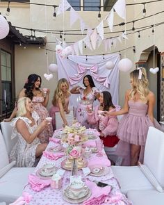 a group of women standing around a table with plates and cups on it, all dressed in pink