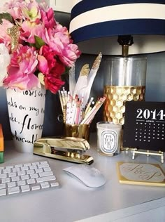 a desk with a keyboard, mouse and flowers in a vase next to a lamp