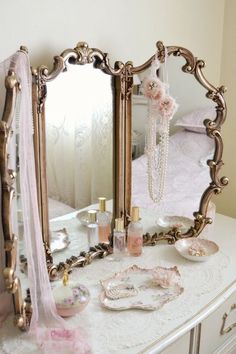 an ornate gold mirror sitting on top of a white dresser next to a pink rose