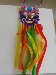 a dragon mask hanging on the wall with colorful streamers around it's neck