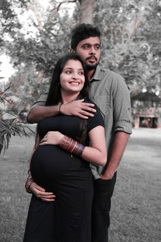 a man and woman standing next to each other in front of a tree with their arms around the pregnant belly