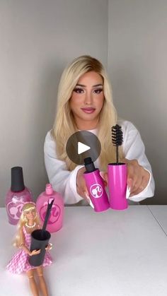 a barbie doll holding a hair dryer next to a pink cup with a brush in it