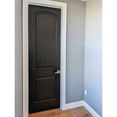 an empty room with a black door and hardwood floors in front of the door is a gray wall