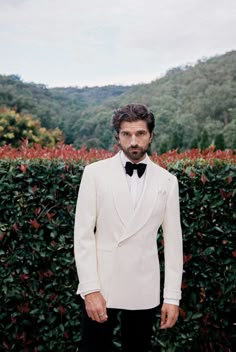 a man in a tuxedo standing next to a hedge