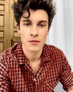 a young man with curly hair wearing a red and white shirt looking at the camera