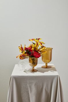 two vases filled with flowers on top of a white table cloth covered tablecloth