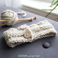 a crocheted headband with two wooden buttons and yarn on the end, next to a pair of knitting needles