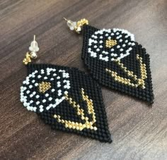 two black and white beaded earrings with gold accents on top of a wooden table