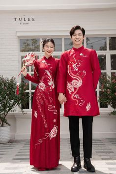 two people standing next to each other in front of a white building with red decorations on it