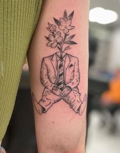 a man in a suit and tie holding a flower tattoo on his left arm,