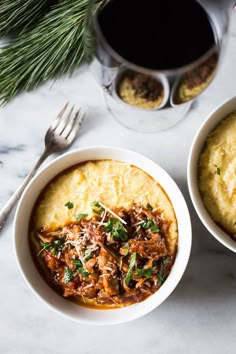 two white bowls filled with food on top of a table next to utensils