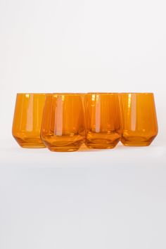 three orange glass cups sitting next to each other on a white surface with no one around them