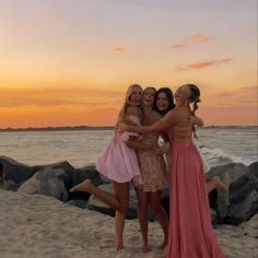 three girls are hugging on the beach at sunset