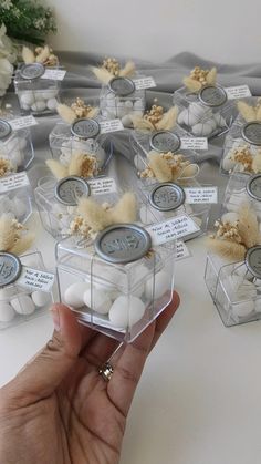 a hand holding a container filled with lots of small white balls next to some flowers