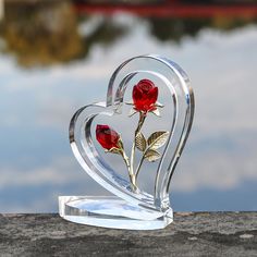 a glass heart shaped sculpture with two roses in the shape of a heart on top of a rock