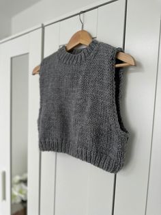 a gray sweater hanging on a white wall next to a pair of wooden hangers