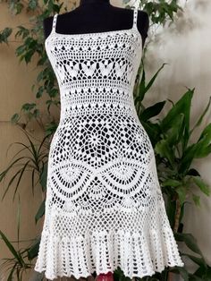 a white crochet dress on a mannequin with plants in the background