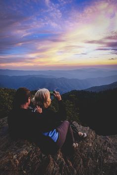 two people sitting on top of a mountain looking at the sky