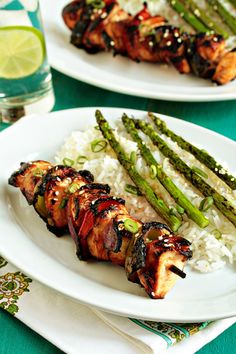 a white plate topped with meat and asparagus covered in sauce next to rice