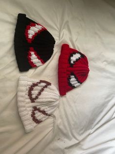 three knitted hats laying on top of a white bed next to an unmade pillow