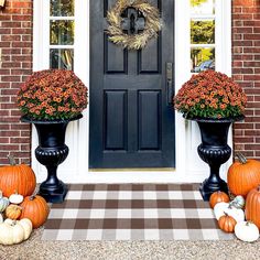 two black urns filled with flowers and pumpkins sitting in front of a door