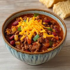 a bowl filled with chili and cheese on top of a table next to crackers