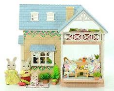 a toy house with two rabbits in front of it and a doll sitting on the floor