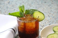 a drink with cucumber slices and mint on the rim next to a napkin