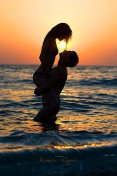 a man and woman kissing in the ocean at sunset