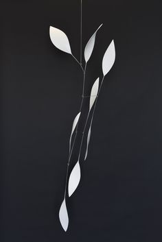 a metal sculpture with white leaves hanging from it's side on a black wall