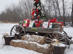 a christmas tree sitting on top of a wooden cart filled with presents next to a pile of hay