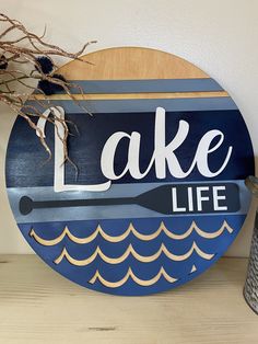 a wooden sign that says lake life on the side of a wall next to a vase with flowers