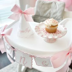 a cupcake sitting on top of a white table with pink ribbon around the edges