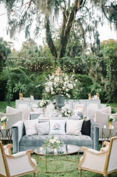 an outdoor seating area with couches, tables and flowers on the table is surrounded by greenery