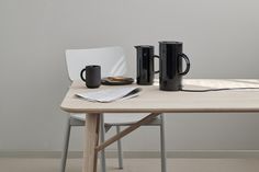 two black mugs sitting on top of a wooden table next to a white chair