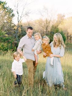 a man and woman holding two small children while standing in tall grass