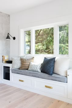 a window seat with pillows on it in front of a wall mounted oven and microwave