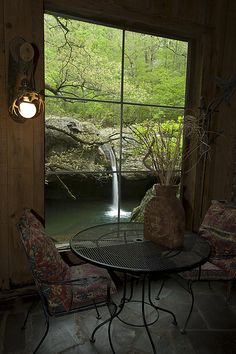 a table and chairs in front of a window with a waterfall coming out of it