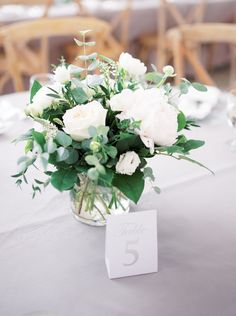 a vase filled with white flowers sitting on top of a table next to a number five sign